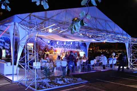 Activación de producto en una carpa iluminada en azul con estructura truss y mesas para invitados