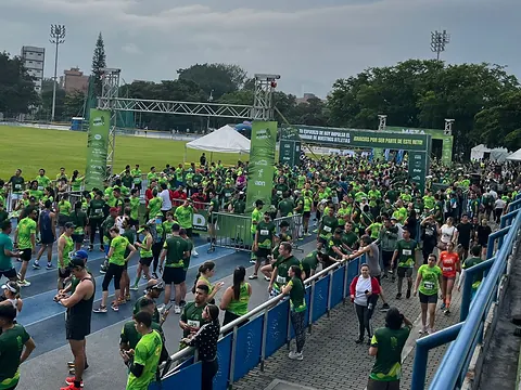 Cientos de corredores de Corro por mi Planeta con camisetas verdes bajo el arco de salida y meta en una pista de atletismo