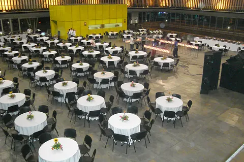 Montaje de banquete con decenas de mesas redondas con mantel blanco y centros de mesa